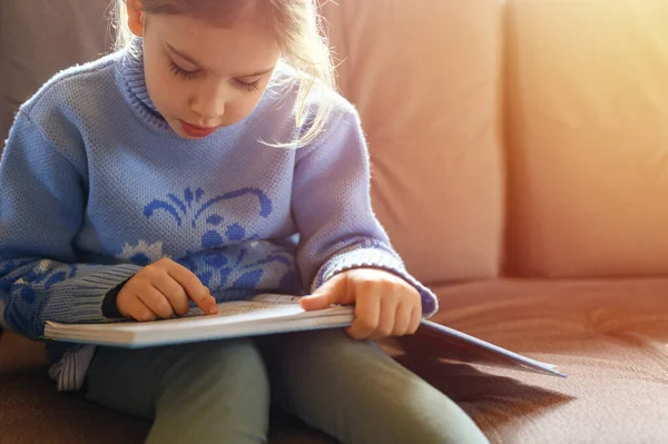 a cute little european kid girl of seven years old reads a book, stay at home during the self isolation of the covid-19 corona virus quarantine. flare