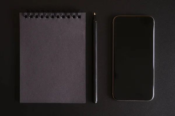 notebook on a spring with black sheets, and a pen, and mobile phone on a black background. space for text