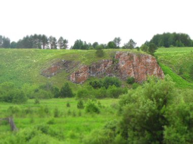 Orman ve tarlalarla çevrili bir kaya.