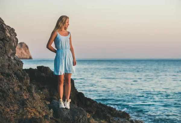 Mujer rubia joven de pie sobre rocas por el mar — Foto de Stock