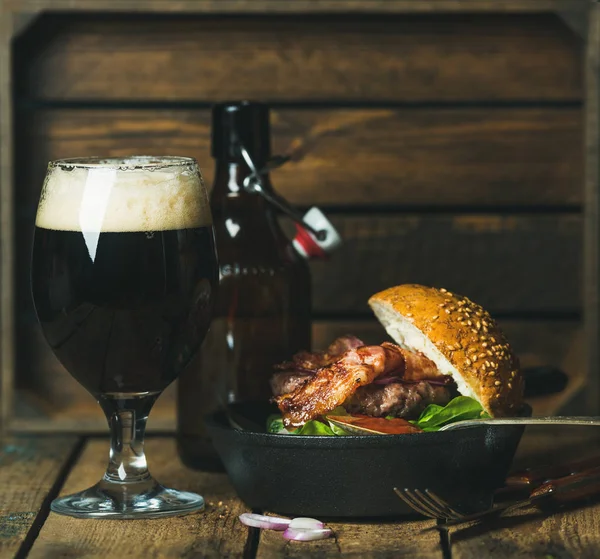 Hovězí burger s křupavou slaninou v pánvi a tmavé pivo — Stock fotografie