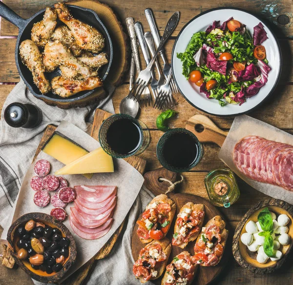 Rustic table set with salad, chicken, brushettas, olives, red wine — Stock Photo, Image
