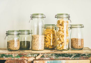 Various uncooked cereals, grains, beans and pasta for healthy cooking in glass jars on rustic table, white background. Clean eating, vegetarian, vegan, balanced dieting food concept clipart