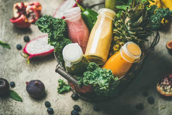 Renkli smoothies ile taze tropikal meyve ve yeşillik sepeti gri beton zemin üzerine şişelerde