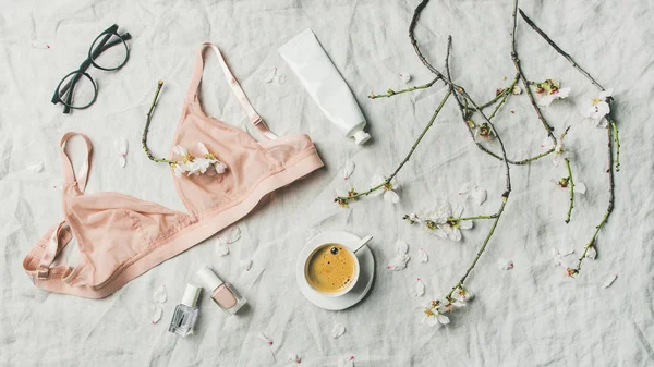 Woman's morning rituals concept. Feminine tender pink lingerie, glasses, cosmetic items, cup of coffee and Spring almond blossom flowers over light grey linen bed cover, top view. — Stock Image Woman Morning Rituals Concept Feminine Tender Pink Lingerie Glasses Cosmetic Royalty Free Stock Photos