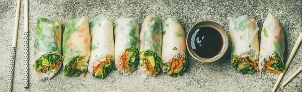 Healthy Asian cuisine. Vegan spring, summer rice paper rolls with vegetables, sauce, chopsticks over concrete background