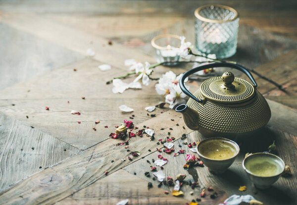 Traditional Asian tea ceremony arrangement. Iron teapot, cups, dried rose buds and candles over wooden table background