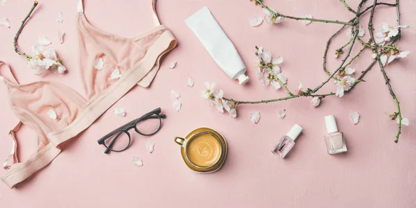 Womans morning rituals concept. Feminine tender powder color lingerie, glasses, cosmetic items, cup of coffee and Spring blossom flowers — Stock Image Womans Morning Rituals Concept Feminine Tender Powder Color Lingerie Glasses Stock Image