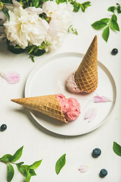Pembe çilek ve Hindistan cevizi dondurma kaşık toz, tatlı koni ve Şakayık çiçekleri buketi beyaz arka plan üzerinde plaka üzerinde