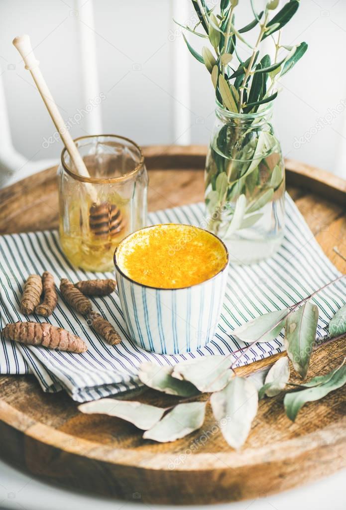 Healthy vegan turmeric latte or golden milk with honey in striped cup on wooden tray