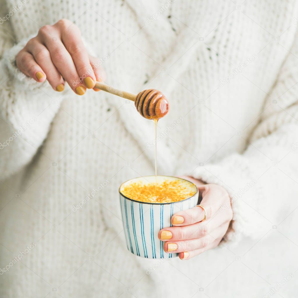 Healthy vegan turmeric latte or golden milk with honey in female hands