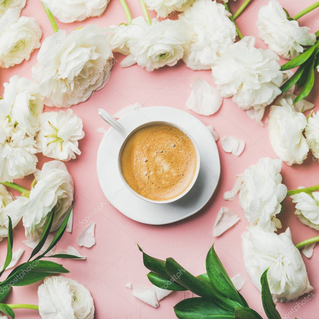 Spring morning concept. Cup of coffee surrounded with white ranunculus flowers over light pink pastel background