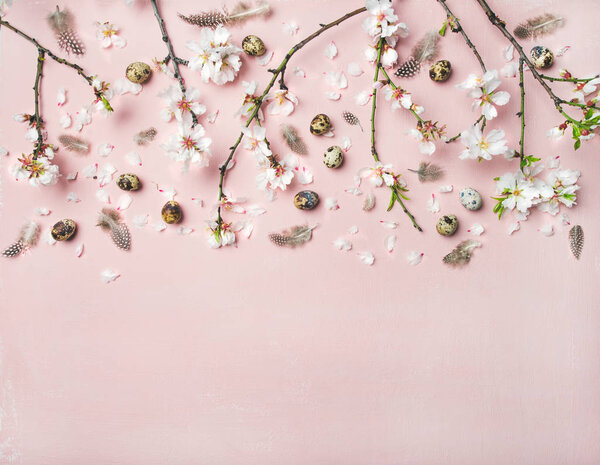 Easter holiday background. Tender Spring almond blossom flowers on branches, feathers and quail eggs over light pink background