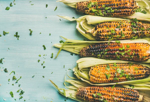 Summer vegan dinner or snack. Grilled sweet corn with smoked sea salt and cilantro over blue background