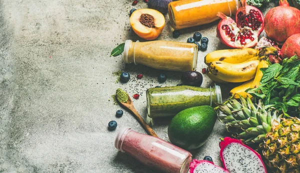 Colorful smoothies in bottles with fresh tropical fruit and superfoods on concrete background