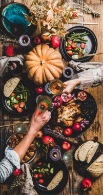 Şükran Günü sofrası. Bayramı şenlik masasında şampanyayla kutlayan çiftler. Kızarmış tavuk, sebze, incirli turta, meyve, ahşap masa arkasında mumlar, üst manzara.