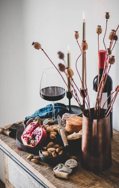 Red wine, appetizers, candles and flowers over wooden kitchen counter — Stock Photo, Image