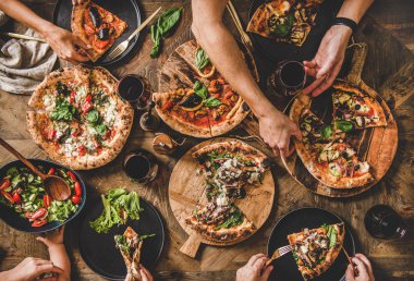 İnsanlar farklı türde pizza yiyor, salata yiyor ve şarap içiyor.