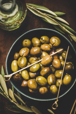Flat-lay of fresh harvested seasonal pickled green Mediterranean olives in bowl over dark rusty background, top view. Healthy snack, starter or traditional meze food
