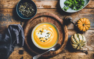 Autumn, winter warming seasonal dinner. Flat-lay of pumpkin soup with seeds, parsley and cream in bowl over rustic wooden background, top view. Vegan, vegetarian, healthy, comfort food concept