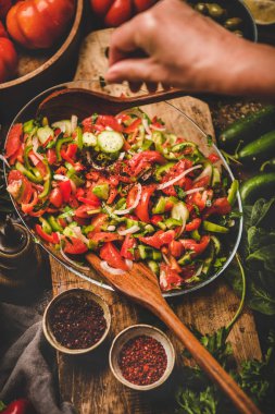 Flat-lay of womans hands adding spices to Turkish Chopard Salad made of fresh vegetables, herbs with olives, top view. Middle eastern, Mediterranean typical cuisine, vegan healthy dish