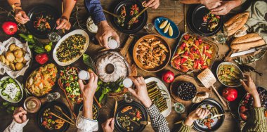 Traditional Turkish celebration dinner. Flat-lay of people eating Turkish salads, cooked vegetables, meze starters, pastries and drinking raki drink, top view, wide composition. Middle Eastern cuisine