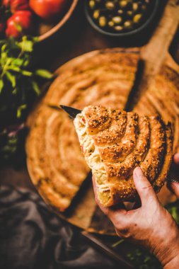 Turkish traditional pastry for breakfast. Human hands holding piece of borek pie with spinach filling and vegetable ingredients over rusty table background, top view, selective focus. Turkish cuisine