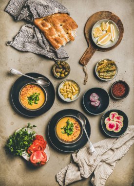 Turkish lentil soup Mercimek. Flat-lay of soup, fresh vegetables, flatbread, pickled peppers, beans, greens and spices over concrete background, top view. Vegetarian, Oriental, Middle Eastern cuisine