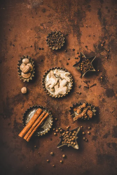 Turkish cuisine seven spice Yedi Bahar mix. Flat-lay of black pepper, ginger, cloves, nutmeg, cinnamon, allspice and alpinia root in vintage tin cookie molds over rusty background, top view