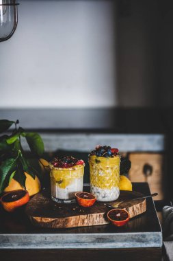 Gri beton mutfak tezgahının üzerinde mango smoothie, karabuğday taneli granola ve taze böğürtlenli gece yulafı, fotokopi alanı. Sağlıklı, temiz yemek, konfor yaşam tarzı konsepti