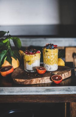 Gri beton mutfak tezgahının üzerinde bir gecelik yulaf ezmesi, mango smoothie, karabuğday taneli granola ve taze böğürtlen. Sağlıklı, temiz yemek, konfor yaşam tarzı konsepti