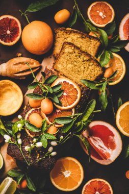 Citrus Akdeniz ekmekli keki. Taze portakallı, limonlu, kumkatlı, greyfurtlu ve çiçekli bademli kek, koyu paslı arka plan, üst manzara. Unsuz vejetaryen tatlı konsepti