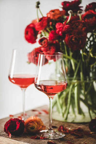 Rose wine in glasses and red spring blossom flowers bouquet over rustic wooden table background, selective focus. Wine shop, bar, wine tasting, wine list concept