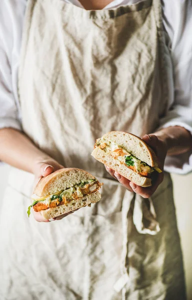 Keten önlüklü kadın elinde tartar soslu taze kızarmış balık sandviçi, limon ve roka dilimleri elinde seçici bir odak noktası tutuyor. Sağlıklı, kolay kahvaltı fikirleri