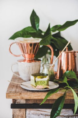 Kahve ve tatlı hazır. Yeşil kibrit peynirli kek ve kırsal ahşap mutfak tezgahında bakır kahve demliğinde demlenmiş kahve, beyaz duvar arkası, yakın plan. Sağlıklı, vejetaryen, vejetaryen, düşük kalorili yiyecekler