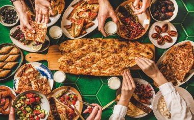 Müslüman Ramazan iftar aile yemeği. Orta Doğu yemek masasında yemek yiyen bir sürü insan. Tarihler, dolma, kebap, yassı ekmek, pide, borek, tatlılar, ayran içeceği, üst manzara. Ramazan oruç tutan Türk mutfağı