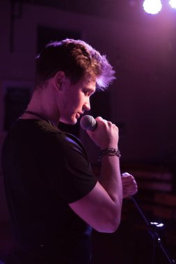 Genç yakışıklı adam duygusal olarak şarkı söylüyor ve mikrofona konuşuyor.