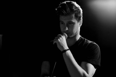 Genç yakışıklı adam duygusal olarak şarkı söylüyor ve mikrofona konuşuyor. Siyah beyaz fotoğraf.