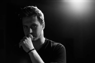 Genç yakışıklı adam duygusal olarak şarkı söylüyor ve mikrofona konuşuyor. Siyah beyaz fotoğraf.