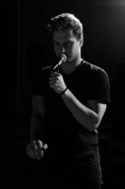 Genç yakışıklı adam duygusal olarak şarkı söylüyor ve mikrofona konuşuyor. Siyah beyaz fotoğraf.