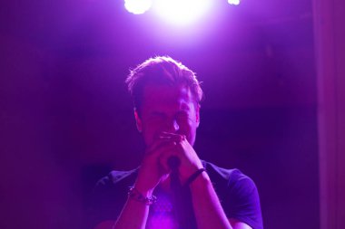 Genç yakışıklı adam duygusal olarak şarkı söylüyor ve mikrofona konuşuyor.