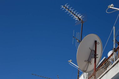 Mavi gökyüzüne karşı çatıda uydu ve televizyon antenleri