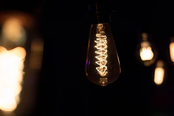 Edison lamp with warm light sways lightly on a black background