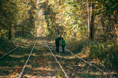 Anne ve oğlu sonbahar ormanında demiryolunun yanında.
