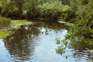 Bir adam ve bir kız kano nehirde kürek çekiyor.