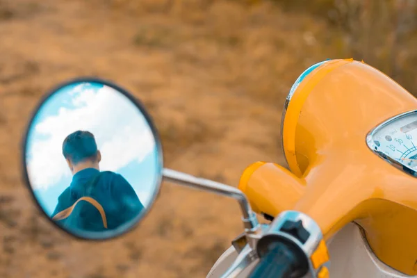 Reflection of a man in the side mirror of a motorbike