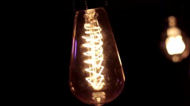 Edison lambasına yakın çekim. Ilık ışık siyah arka planda hafifçe sallanıyor.