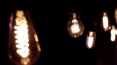 Edison lambasına yakın çekim. Ilık ışık siyah arka planda hafifçe sallanıyor.