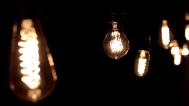 Edison lambasına yakın çekim. Ilık ışık siyah arka planda hafifçe sallanıyor.
