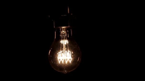 暖かい光が黒の背景に軽く揺れるエジソンランプのクローズアップ — ストック動画